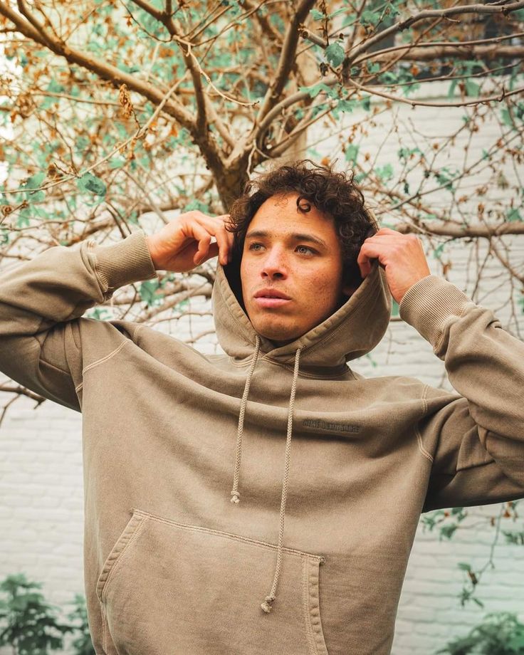 a man in a brown hoodie standing next to a tree