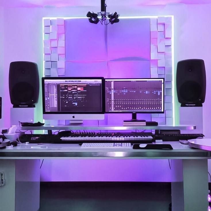 a computer desk with two monitors and speakers on it in front of a purple wall