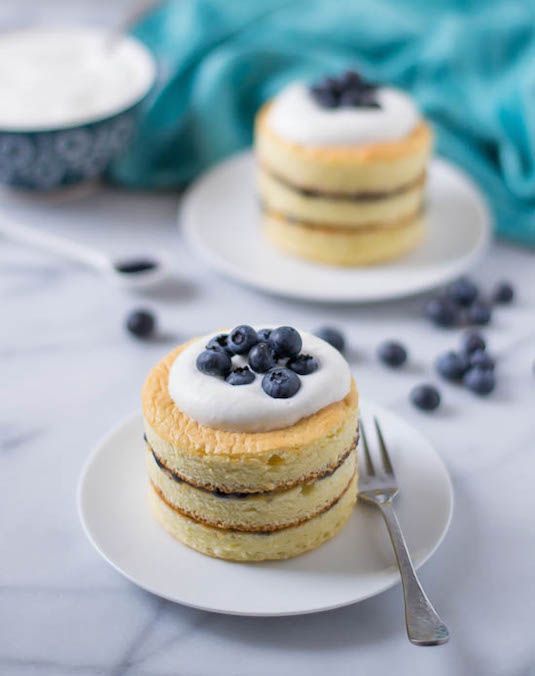 two small cakes with blueberries on top are sitting on plates next to each other