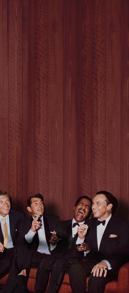 four men in tuxedos are sitting on a couch and drinking wine together,