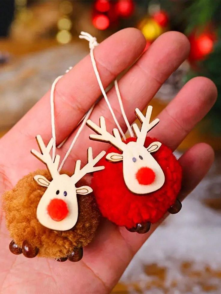 two red and white reindeer earrings hanging from strings on a person's hand in front of a christmas tree