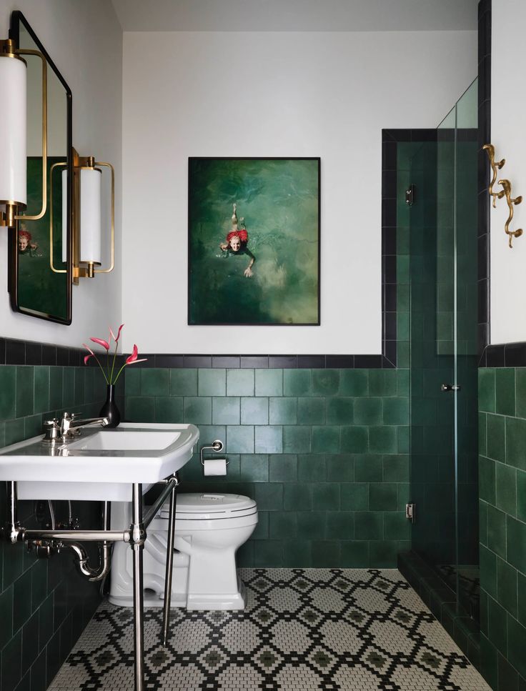 a bathroom with green tile and black and white tiles on the floor, along with a painting above the toilet