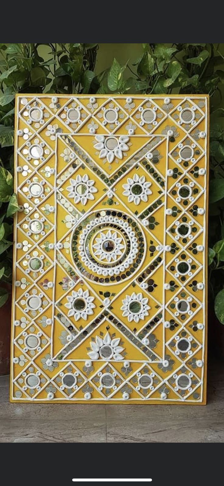 a yellow and white tile with an intricate design on it's side, next to some potted plants