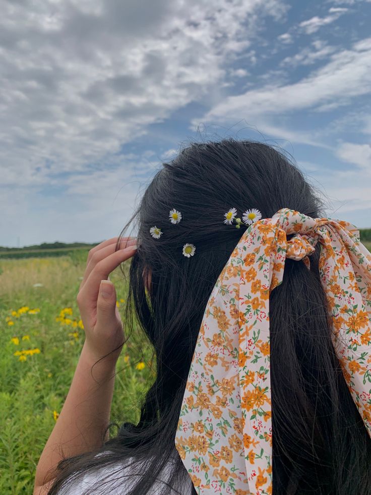 a woman with her hair tied back in a flowery headband, standing in a field