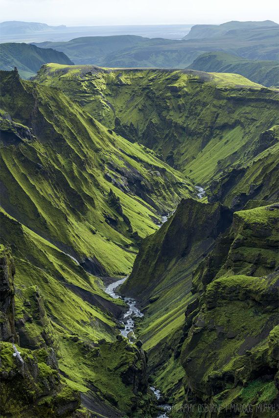 the green mountains are very high up in the sky and there is a river running through them