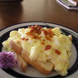 a plate topped with toast and eggs next to a purple flower on a wooden table