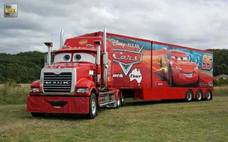 a large red truck with cars painted on it's sides parked in a field