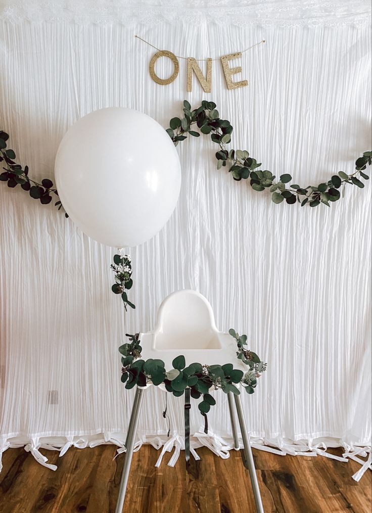 two white chairs sitting on top of a wooden floor next to a one balloon sign