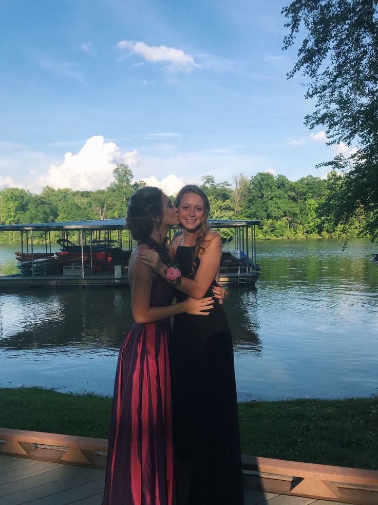 two women standing next to each other in front of a lake with boats on the water