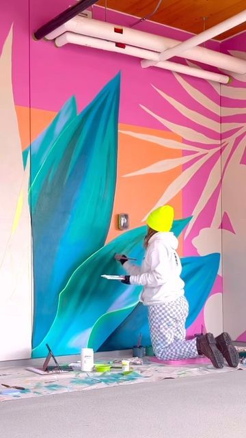 a woman painting a mural on the side of a wall in a room with pink and blue walls