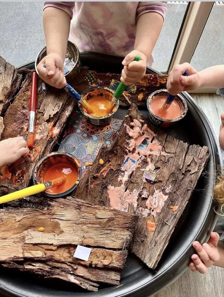 several children are painting on wood with paintbrushes and watercolors in their hands