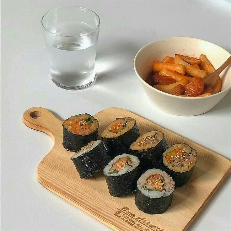 sushi on a cutting board next to a bowl of fries and a glass of water