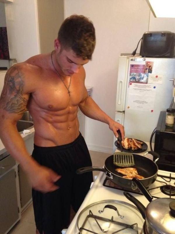 a shirtless man frying food on top of a stove in a kitchen next to a refrigerator