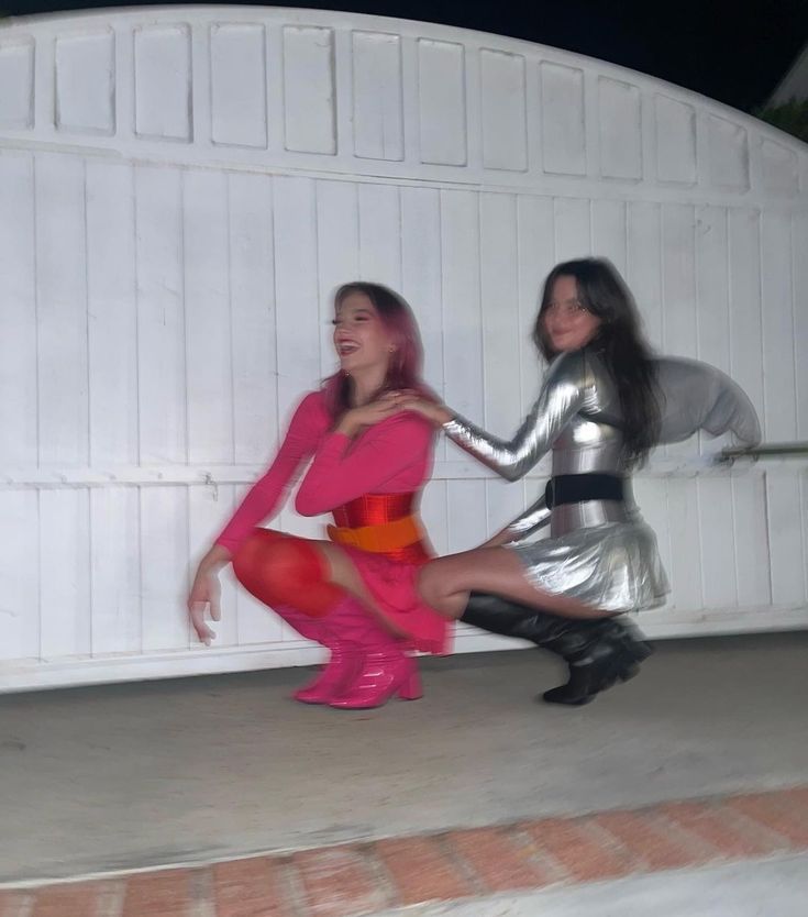 two women dressed in silver and pink posing for the camera with their legs spread out