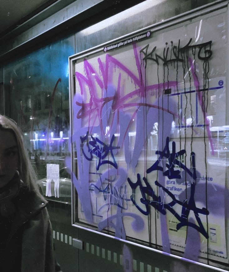 a woman standing in front of a window covered in purple and black grafitti