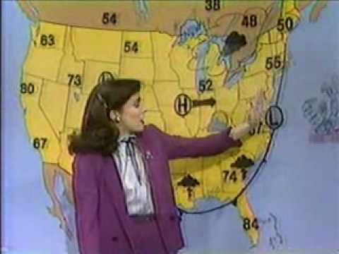 a woman standing in front of a weather map and pointing to the direction on it