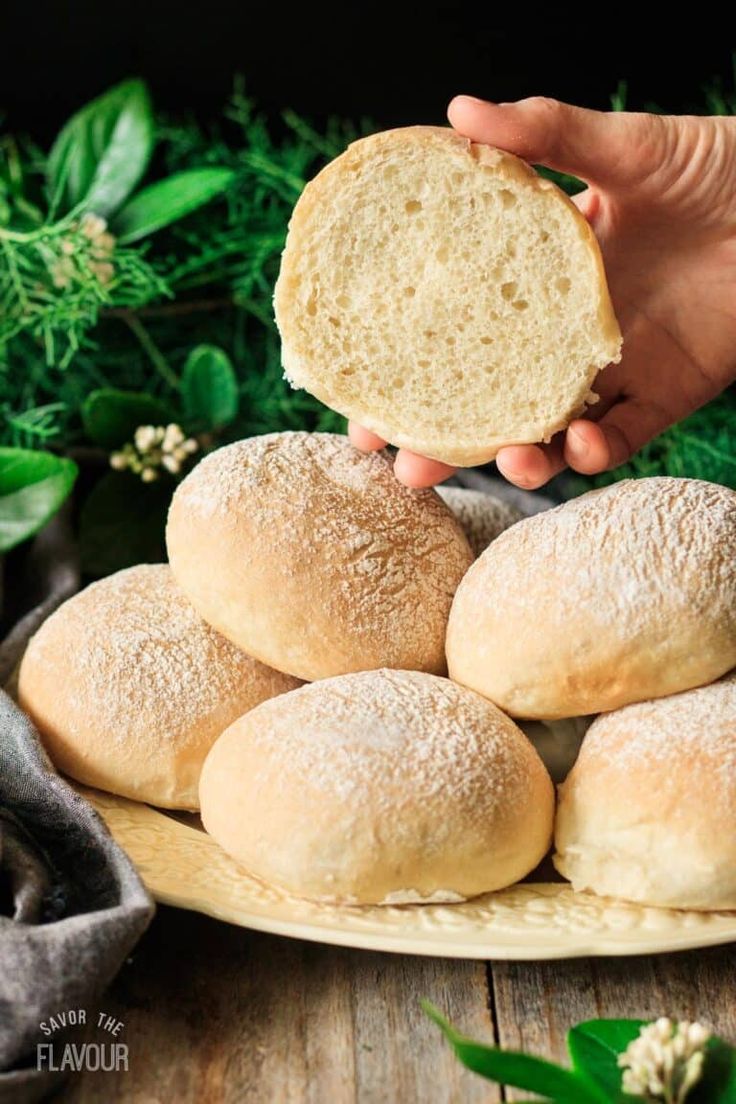 a person holding a piece of bread in front of some buns on a plate