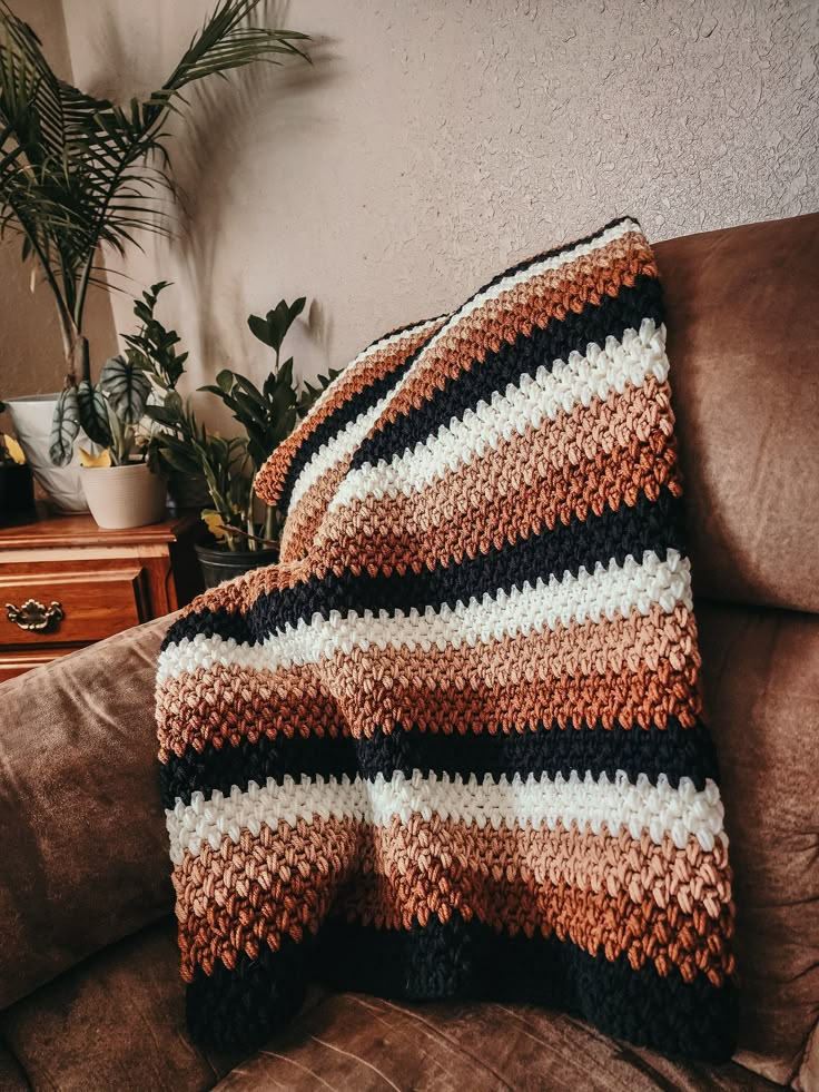 a crocheted blanket sitting on top of a couch next to a potted plant