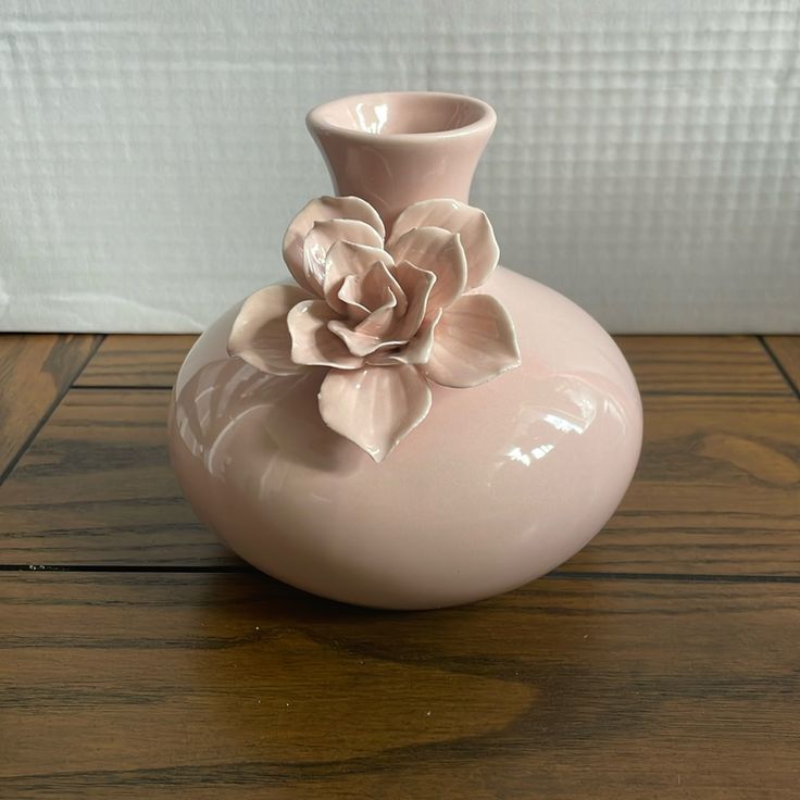 a pink vase sitting on top of a wooden table with a flower in the middle