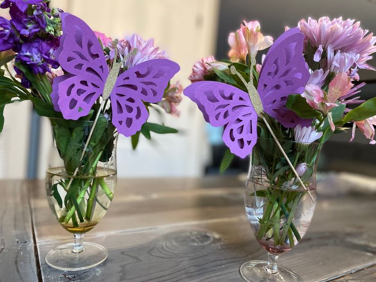 two vases filled with purple flowers sitting on top of a wooden table next to each other