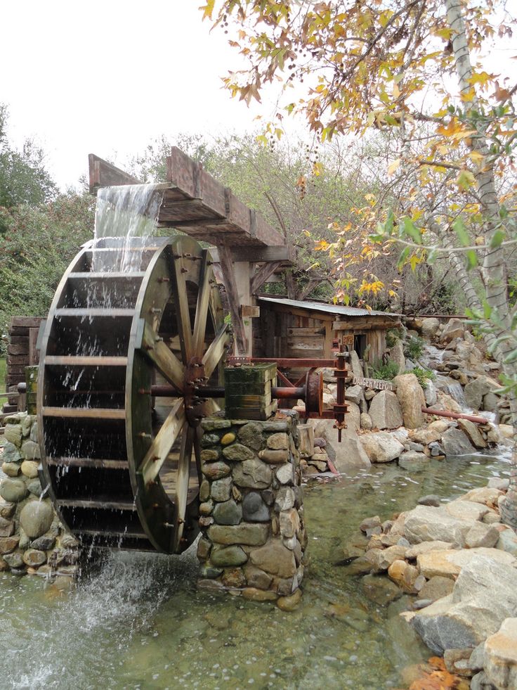 an old mill with water pouring out of it's front wheel and surrounded by rocks