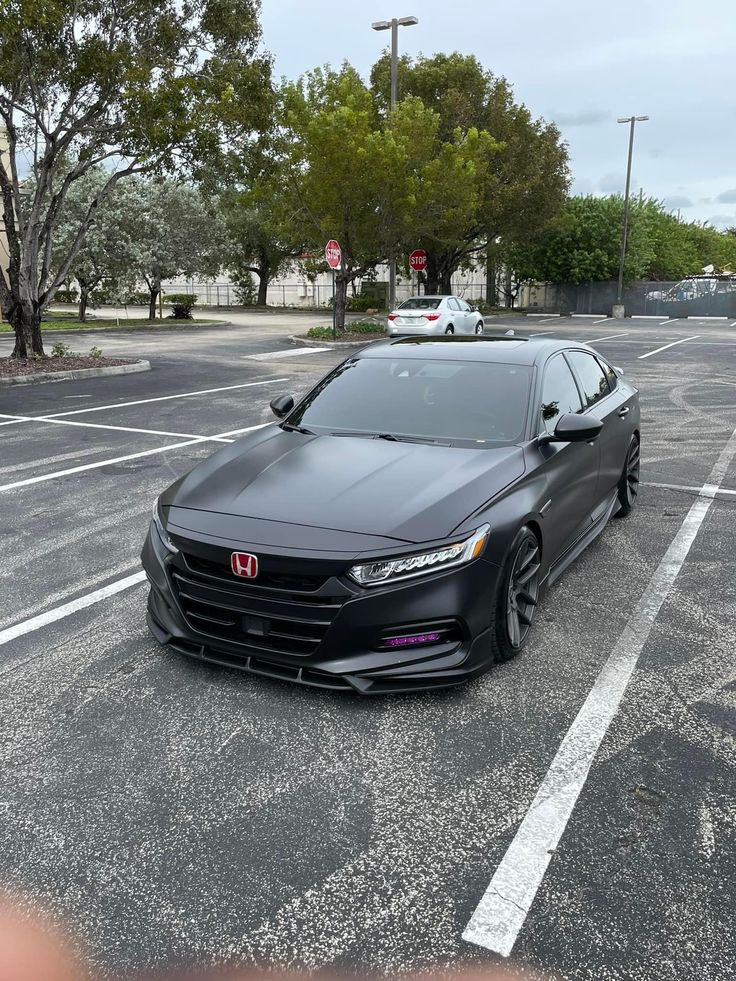 a black car parked in a parking lot next to a red traffic light and trees