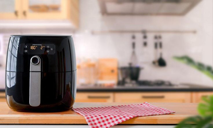 a black air fryer sitting on top of a wooden counter next to a red and white checkered napkin