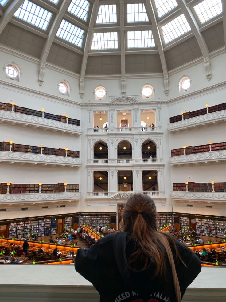 a woman is standing in the middle of a large building with lots of bookshelves