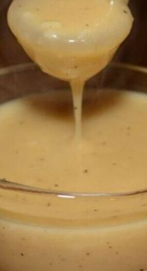 a spoon full of liquid being poured into a glass bowl filled with batter or sauce