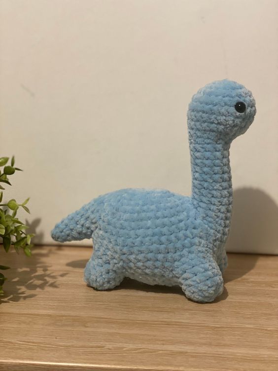 a crocheted blue llama sitting on top of a wooden table next to a potted plant