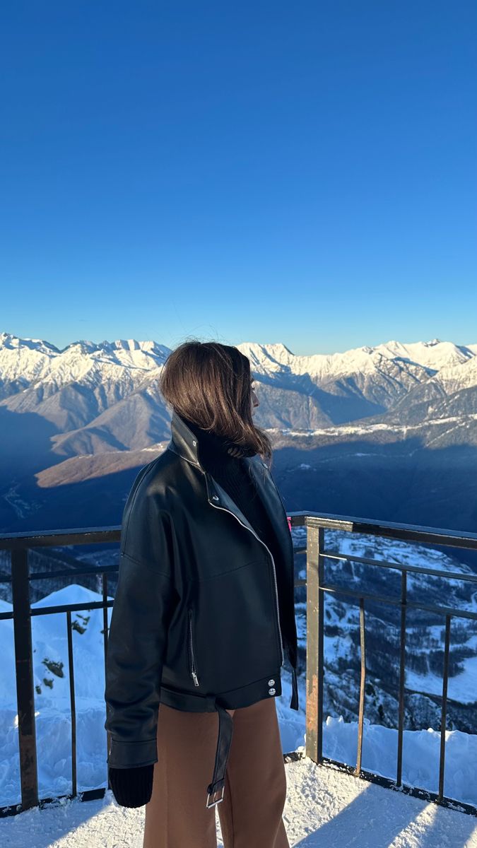 a woman standing on top of a snow covered slope next to a railing with mountains in the background