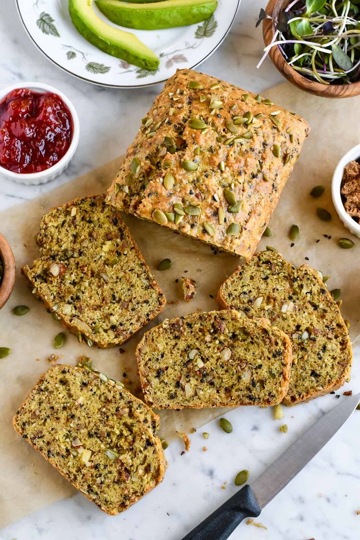 slices of bread sitting on top of a cutting board next to bowls of fruit and vegetables