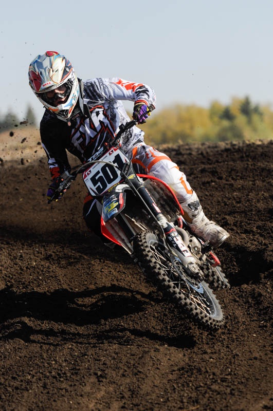 a man riding on the back of a dirt bike down a dirt field covered in dirt