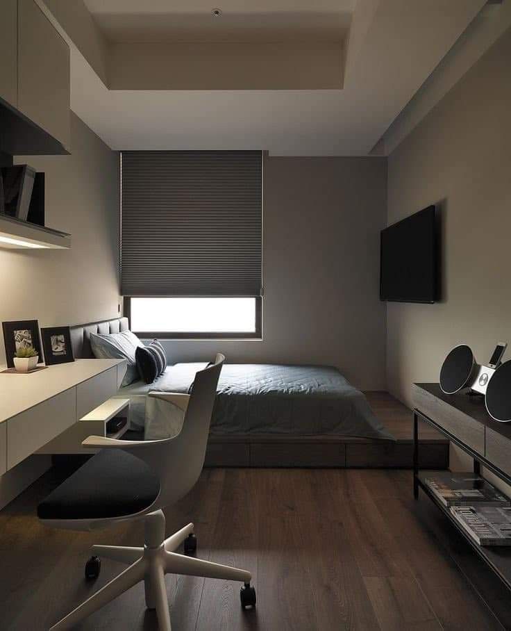 a bedroom with a bed, desk and television on the wall next to it's windows