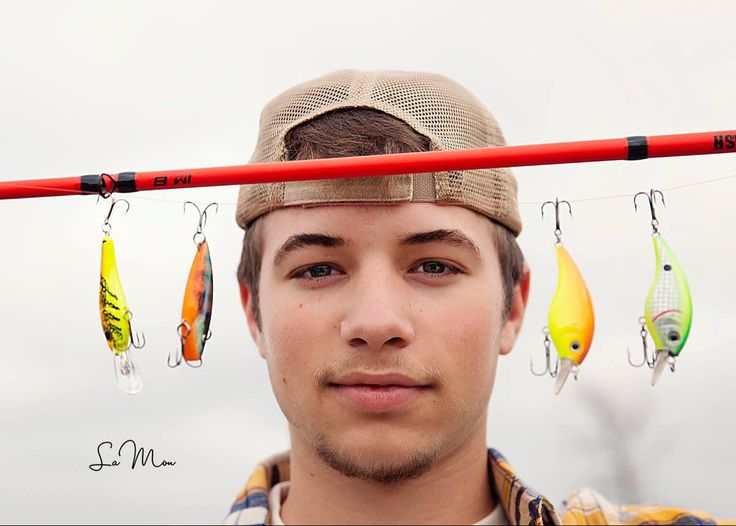 a young man wearing a hat and holding fishing hooks in front of his head,