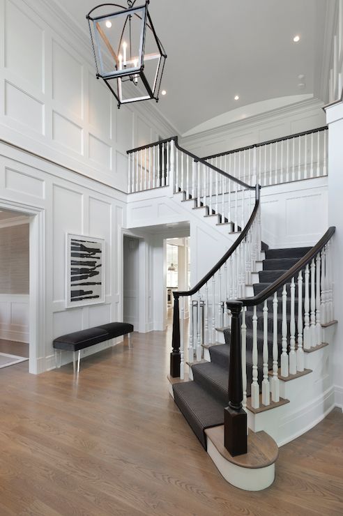 a staircase in a large white house with wood flooring and black handrails