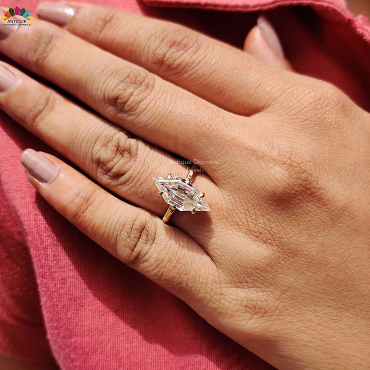 a woman's hand with a diamond ring on her left hand and a pink shirt