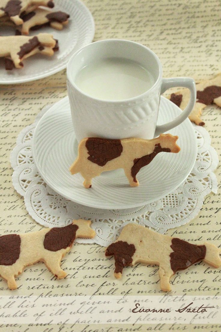 cookies shaped like cows and milk are sitting on a saucer next to a cup