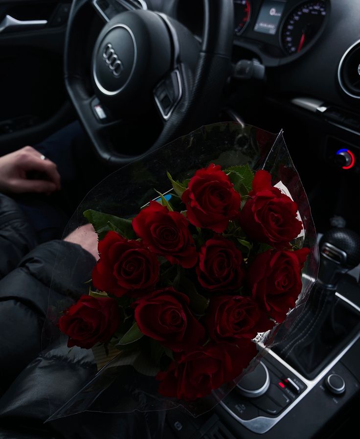 a bouquet of red roses sits in the center console of a car, while someone is driving