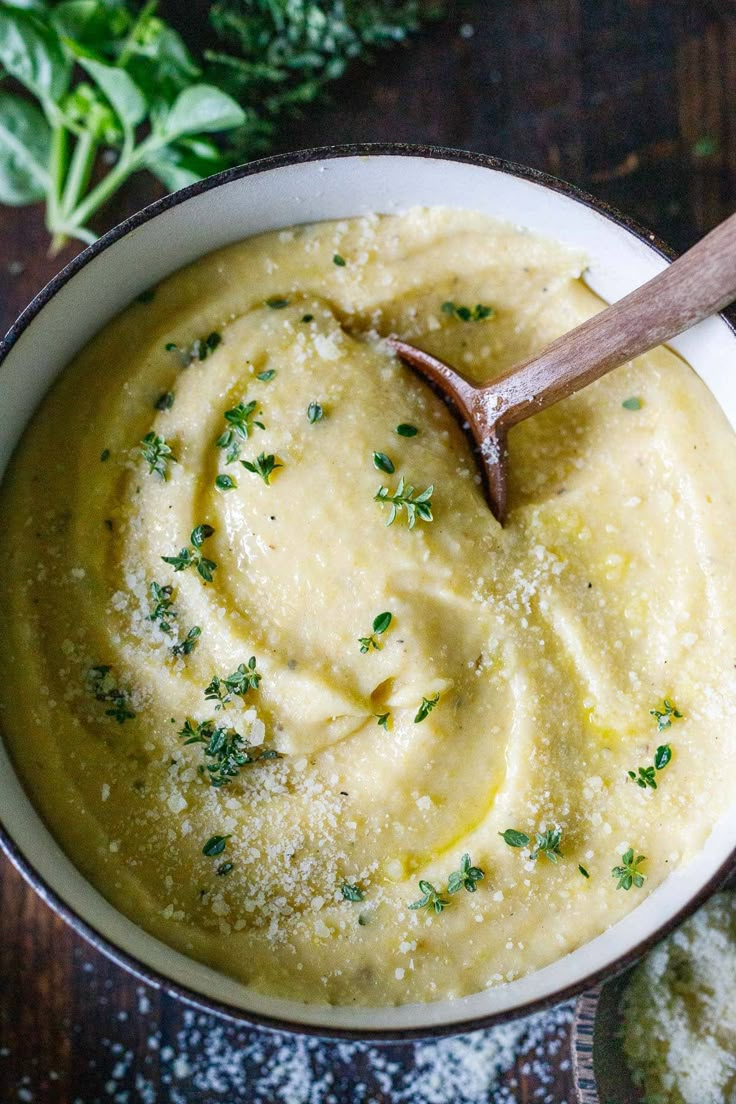 a white bowl filled with mashed potatoes and parsley on top of a wooden table