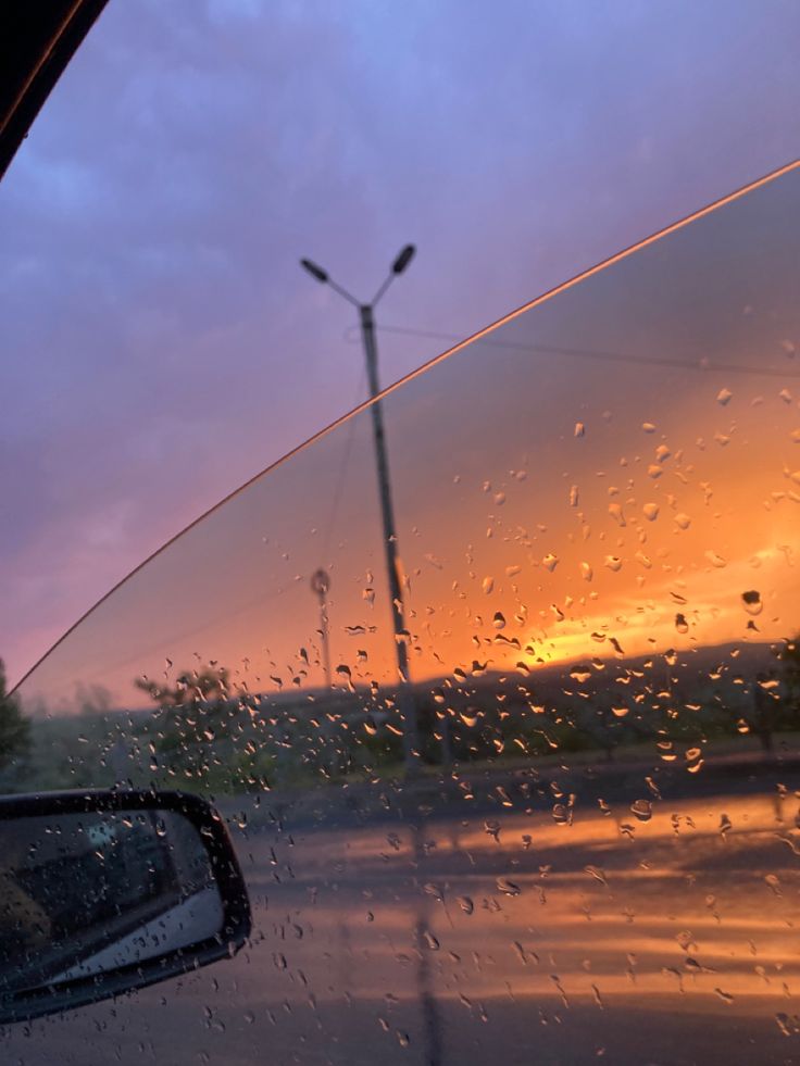 rain drops on the windshield of a car as the sun sets