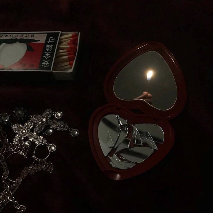 an open mirror sitting on top of a table next to a candle and some jewelry