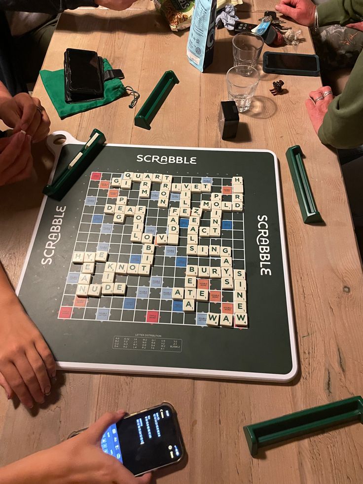 people playing scrabble on a tabletop with their cell phones and gadgets