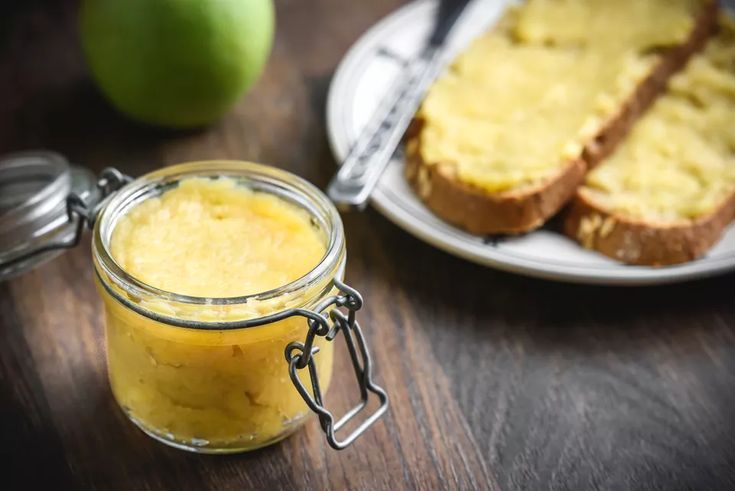 a glass jar filled with food sitting on top of a wooden table next to two slices of bread