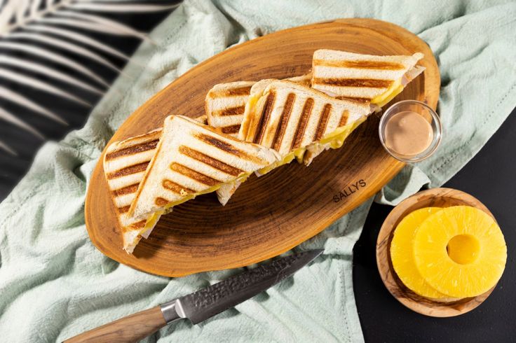 grilled cheese sandwiches on a wooden plate with a glass of orange juice next to it