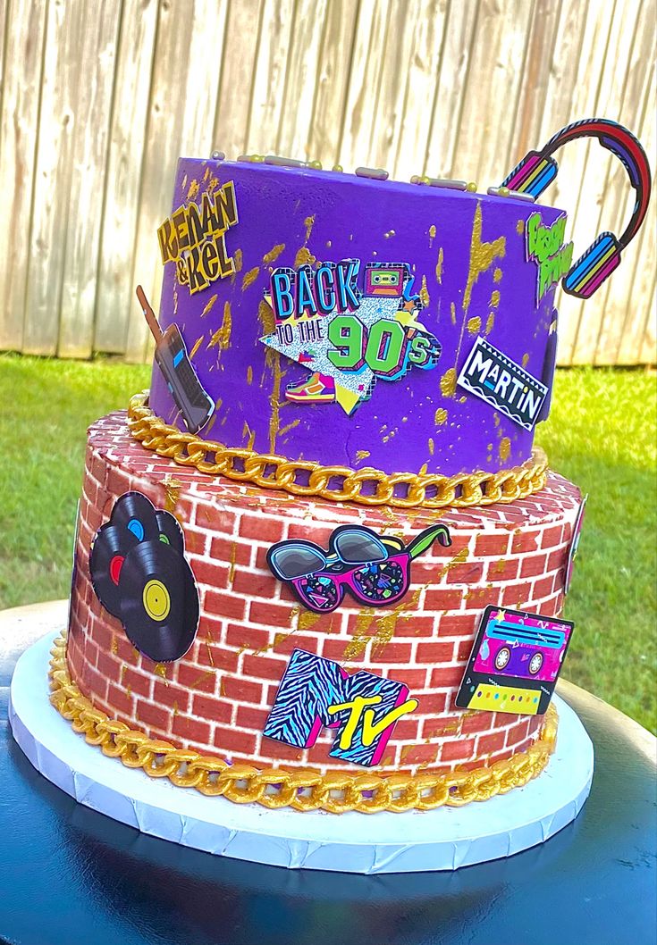 a three tiered cake decorated with stickers on top of a blue table in front of a fence