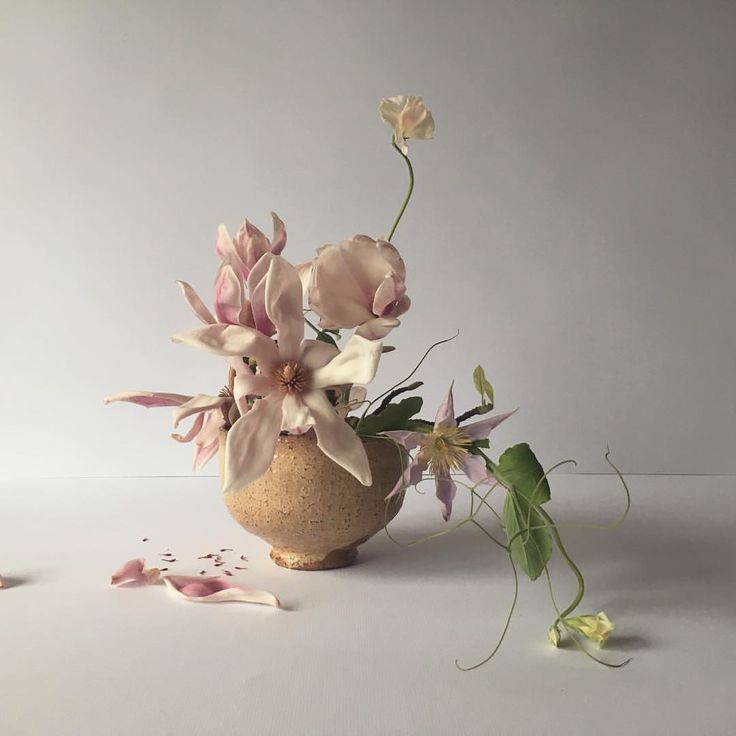 a vase filled with lots of flowers on top of a white table next to leaves