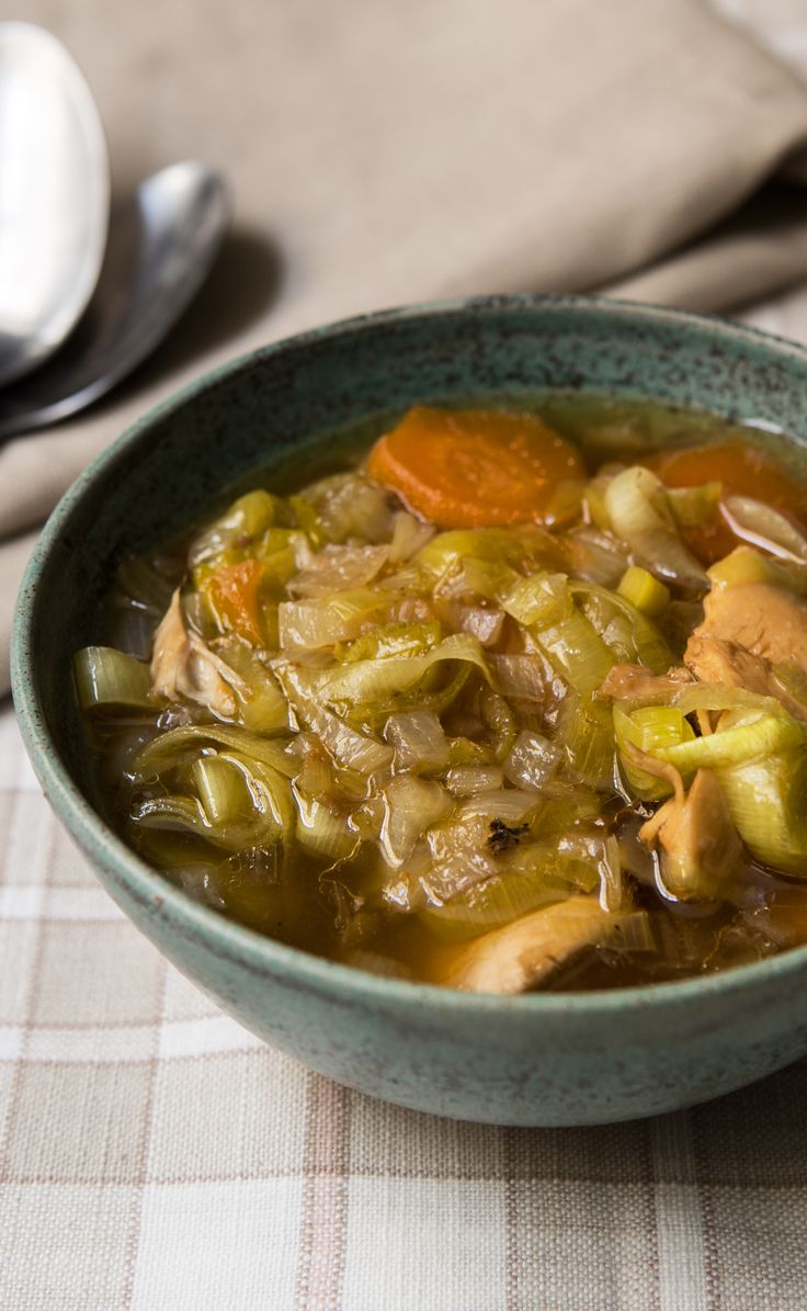 a bowl of soup with carrots, celery and onions on a table