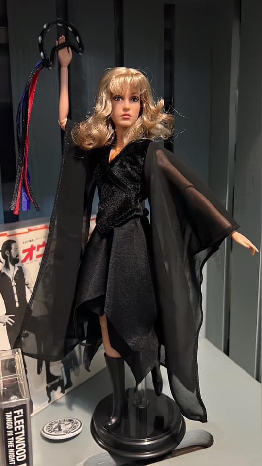 a barbie doll dressed in black and holding a bat on top of a table next to a book