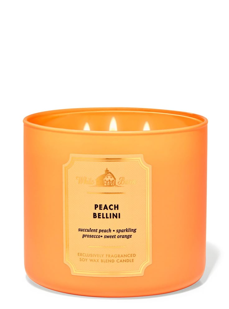 an orange candle is sitting on a white surface with the words peach bellini written in gold